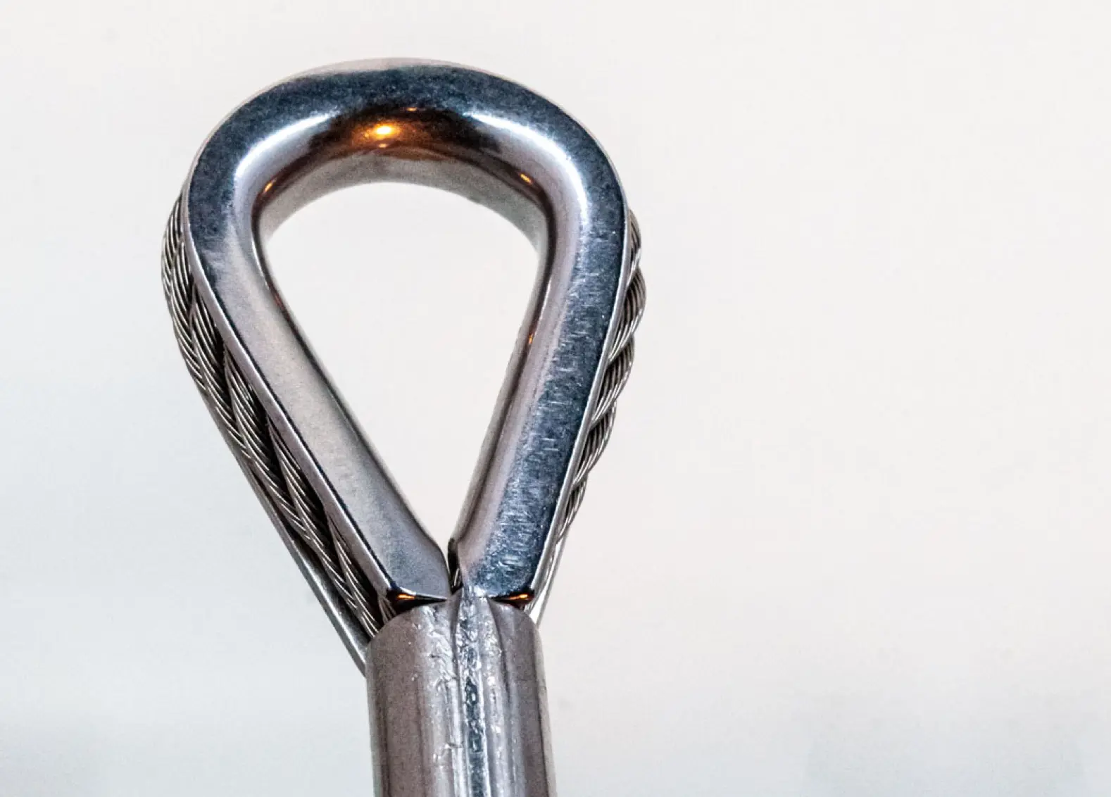 Thimble end fitting with wire rope through it on white background.