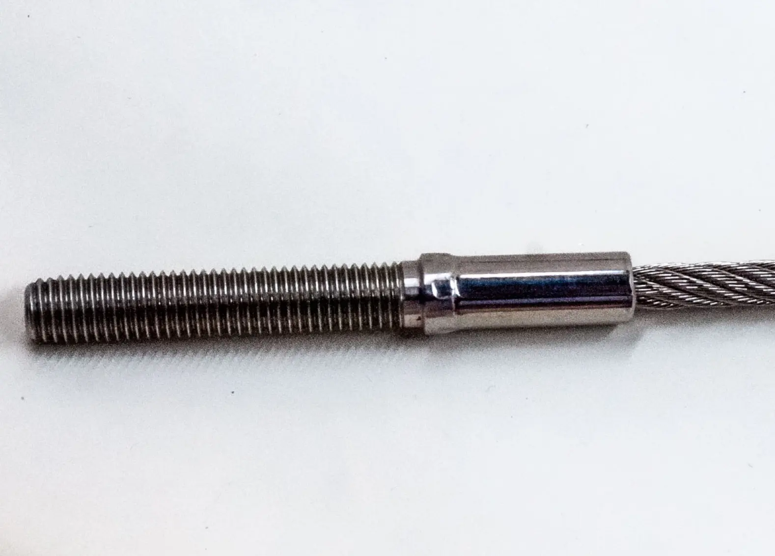 Close of of a threaded stud end fitting attached to a wire rope, on a white background.