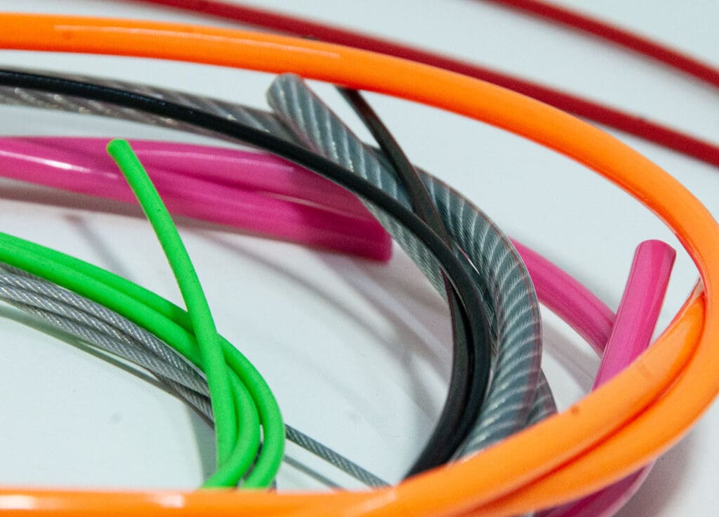 Colorful bundle of custom coated wire rope cables, showcasing the wide variety of vibrant vinyl and nylon jacket color options available for mechanical assemblies.